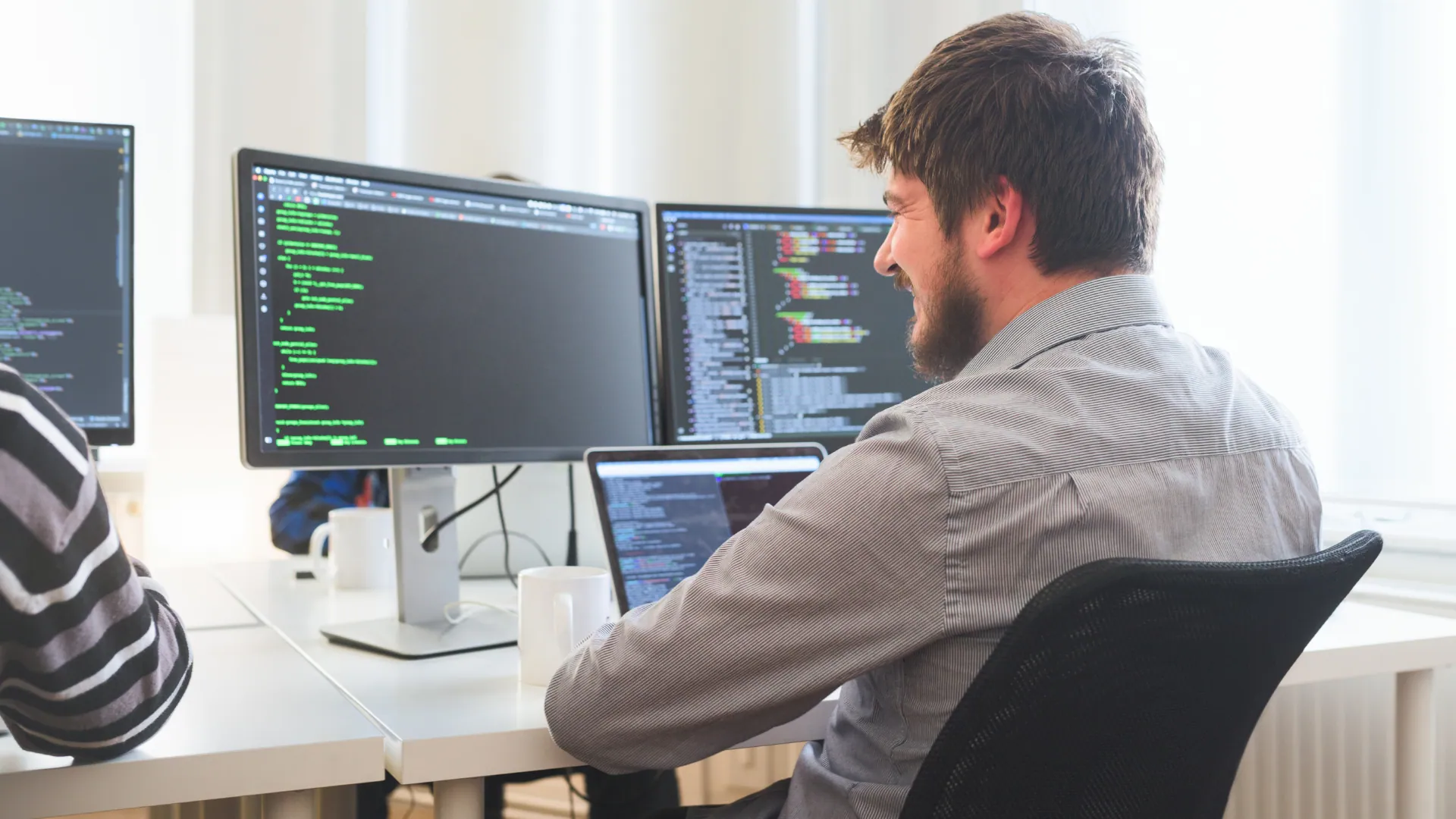 Desarrollador de software trabajando frente a varios monitores con código en una oficina luminosa